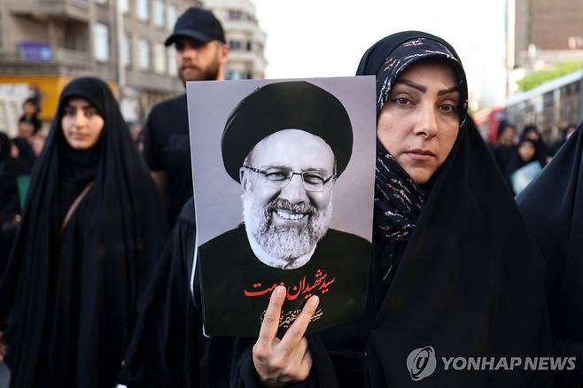 라이시 추모 (테헤란 AFP=연합뉴스) 22일(현지시간) 이란 테헤란에서 열린 에브라힘 라이시 대통령의 장례행렬에 참여한 시민이 라이시 대통령의 사진을 들고 있다. 2024.5.22
