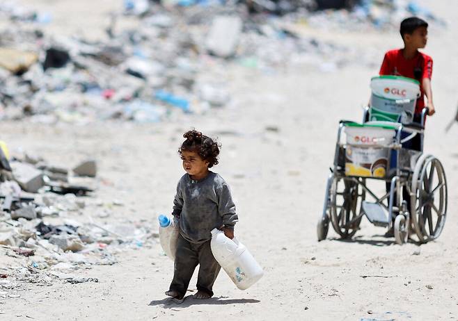 2024년 5월22일 양손에 물통을 든 어린이가 팔레스타인 땅 가자지구 남부 칸유니스의 거리를 걷고 있다. REUTERS 연합뉴스