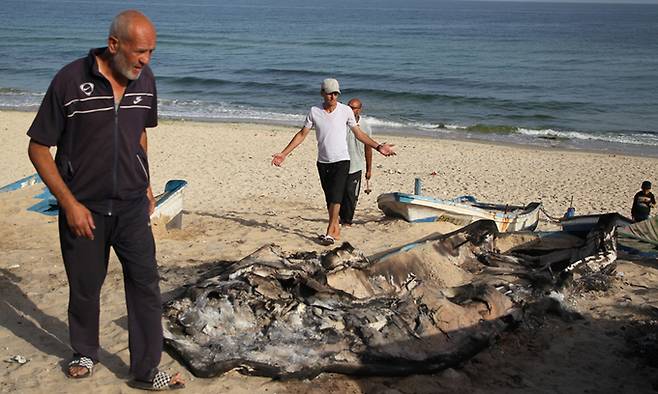 22일(현지시간) 가자지구 남부 도시 라파의 지중해 연안에서 팔레스타인 주민들이 이스라엘의 공습으로 불에 탄 어선 잔해를 살피고 있다. 신화뉴시스