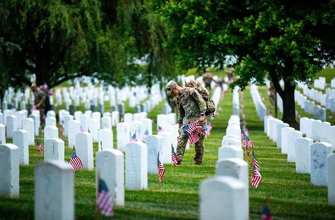 2023년 5월 미국 수도 워싱턴 인근 알링턴 국립묘지에서 미 육군 장병들이 현충일을 앞두고 전몰요사들의 묘비를 성조기로 장식하고 있다. 미 육군 홈페이지