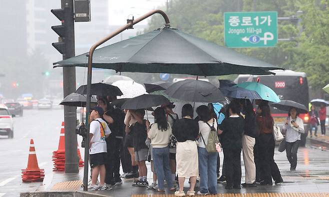 26일 오후 비가 내리는 서울 광화문광장에서 시민들이 파라솔 아래 우산을 쓴 채 보행신호를 기다리고 있다. 연합뉴스
