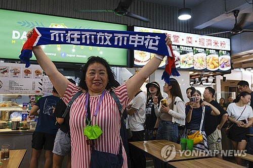 한 중국 축구팬이 14일 싱가포르 축구 국가대표팀 골키퍼 하산 서니가 운영하는 노점 식당 앞에서 포즈를 취한 모습. [AP=연합뉴스]