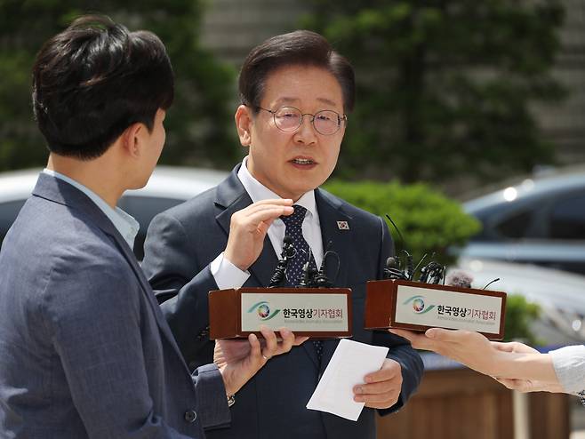 Main opposition leader Lee Jae-myung (right) talks to reporters as he arrives at the Seoul Central District Court in southern Seoul to attend a hearing on election law violations on Friday. (Yonhap)