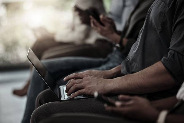 ▲무릎 위에 올린 노트북에 무언가를 적는 사람과 휴대전화를 보는 사람 등이 나란히 앉아 있는 이미지. 사진=Getty Images Bank