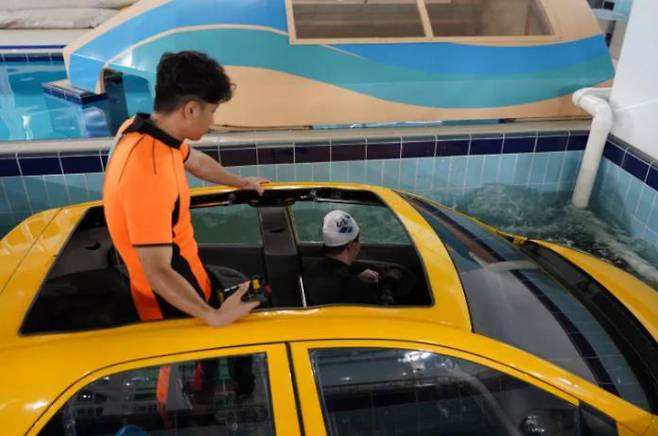 A reporter (right) practices escaping from a submerged vehicle at the Chungbuk Safety Experience Center in Cheongju, North Chungcheong Province, on July 1.  Courtesy of the Chungbuk Fire and Rescue Headquarters