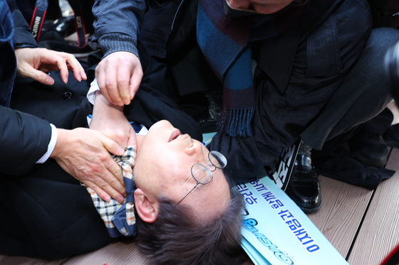 Democratic Party leader Lee Jae-myung lies on the ground after being stabbed during his visit to the site of the new international airport on Gadeok Island, Busan, on Jan. 2. [YONHAP]