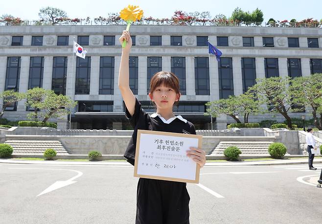 한국 정부의 기후변화 대응이 헌법에 합치하는지를 묻는 기후소송 두번째 공개 변론이 열린 지난 5월21일 오후 서울 재동 헌법재판소 앞에서 청구인 진술자 3인 중 한명인 한제아 아기 기후소송 청구인이 최후 진술문과 함께 ‘반드시 행복은 오고야 만다’는 꽃말의 마리골드 종이꽃을 손에 들고 있다. 백소아 기자 thanks@hani.co.kr