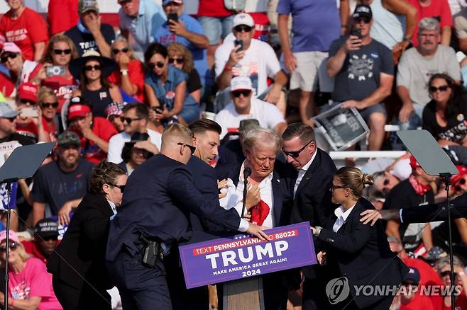 총격 후 얼굴에 피를 흘린 채 경호요원들에게 둘러싸여 연단을 내려오는 트럼프 전 미국 대통령 [로이터=연합뉴스]