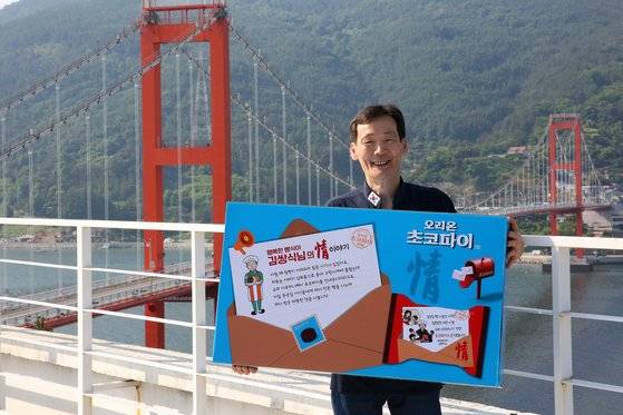 남해 행복 베이커리 김쌍식 대표. 김 대표가 자신의 사연과 얼굴을 새긴 초코파이 박스를 들고 남해대교 앞에 서서 포즈를 취했다. 손민호 기자