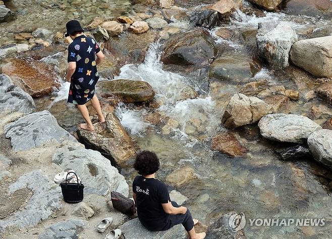 지난 25일 오후 충남 공주시 반포면 계룡산 동학사 계곡을 찾은 시민들이 계곡물에 발을 담그고 있다. 연합뉴스