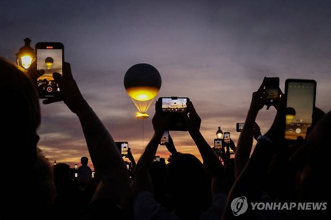 파리올림픽 열기구 성화대 (파리 로이터=연합뉴스) 4일(현지시간) 밤 파리 시내 상공 위로 떠오른 열기구 성화대를 찍는 시민들. 2024.08.11