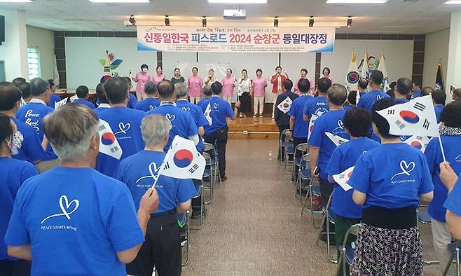 18일 전북 순창군 순창읍사무소 강당에서 열린 한반도와 세계 평화를 염원하는 ‘신통일한국 피스로드 2024 순창군 통일 대장정’에서 각계 지도자 등 100여명의 참석자들이 태극기를 손에 든 채 통일의 노래를 합창하고 있다.