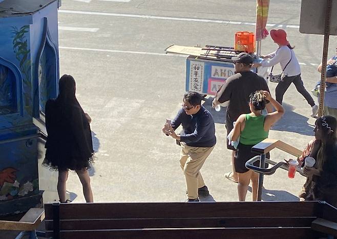 HYBE Chairman Bang Si-hyuk kneels to take a photo of a woman at his multi-billion-won estate in Los Angeles, in this image from an online community. The woman is reportedly AfreecaTV streamer Seyeon’s older sister, who is said to be a friend of Bang. Bang, who had not been appearing in public, introduced the sisters to local dining spots during their visit to the U.S.