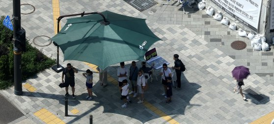 폭염이 이어진 20일 서울 시청역 인근 그늘막 아래에서 시민들이 건널목 신호를 기다리고 있다. 뉴스1