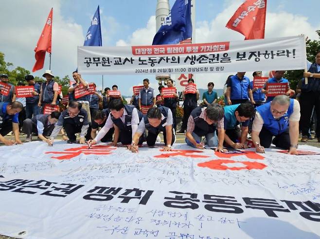 경남지역 공무원·교원 생존권 쟁취 공동투쟁위원회 소속 11개 노조 대표들이 대형 현수막에 요구 내용을 쓰고 있다. [사진=이세령 기자]