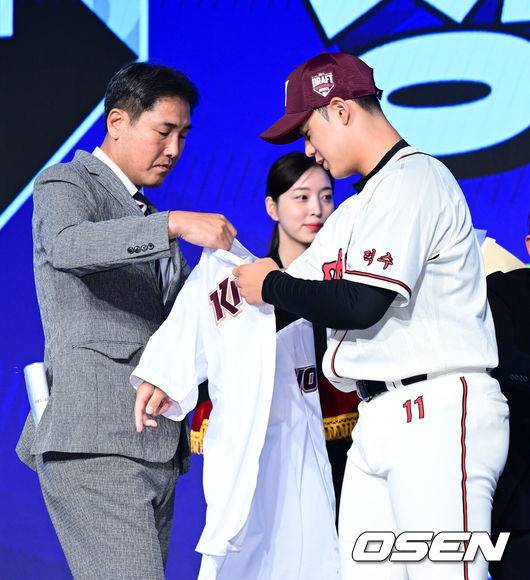 [OSEN=지형준 기자] 11일 오후&nbsp;서울 잠실 롯데호텔 월드에서 2025 KBO 신인 드래프트가 열렸다.2025 KBO&nbsp;신인 드래프트는 전면 드래프트 방식으로 진행된다. 지명은 1라운드부터 11라운드까지 이뤄지며, 2023년도 구단 순위의 역순인 키움-한화-삼성-롯데-KIA-두산-NC-SSG-KT-LG 순서로 실시된다.덕수고 정현우가 전체 1순위로 키움에 지명되며 고형욱 단장에게 유니폼을 건네받고 있다. 2024.09.11 /