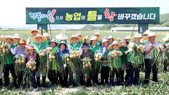 지난 5월 23일 경북 문경시 영순면 공동영농단지에서 ‘경북 농업대전환 공동영농 성과 보고회’가 열린 가운데 참석자들이 농민들과 함께 수확한 양파를 들고 기념촬영하고 있다. 사진 경북도