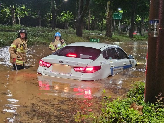 지난 21일 오전 충북 청주시 석소동에서 집중호우로 인해 도로가 침수되어 출동한 소방대원들이 고립된 택시차량을 이동조치하고 있다. 연합뉴스=소방청