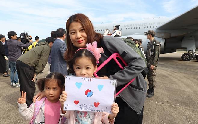 After disembarking from a military transport aircraft at Seoul Air Base on Saturday afternoon, following their departure from Lebanon on Friday, children hold up a sign featuring the South Korean national flag design that reads: "Republic of Korea and soldiers, we love you. We're fine now. Thank you for coming to save us." (Yonhap via Pool Photo)