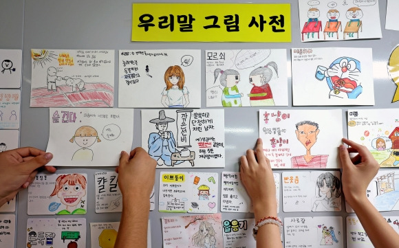 슬겁다·이쁘둥이… 한글날, 우리말 그림 사전으로 기념 - 한글날을 이틀 앞둔 7일 대구 북구 복현중학교에서 학생들이 직접 만든 ‘우리말 그림 사전’ 카드를 교사들이 게시판에 붙이고 있다. 9일 578돌 한글날을 맞아 전국에서 다양한 행사가 열리는 가운데 서울시는 이날 광화문광장 세종대왕상 앞에서 ‘한글 창제 원리 탐방’ 특별 강연 등 다양한 시민 참여 프로그램을 운영할 예정이다. 대구 뉴시스