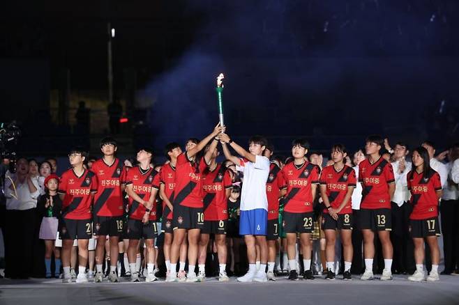 제105회 전국체전 개회식의 성화봉송 최종 주자인 여민지 선수와 진주여중 축구부 선수들이 성화를 들어 보이고 있다. [사진제공=경남도청]