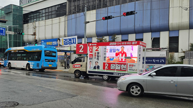 10·16 부산 금정구청장 보궐선거가 치러지는 금정구 장전동 장전역 앞에서 윤일현 국민의힘 후보 유세차가 김경지 더불어민주당 후보의 현수막 아래를 지나가고 있다. 부산=정상훈 기자