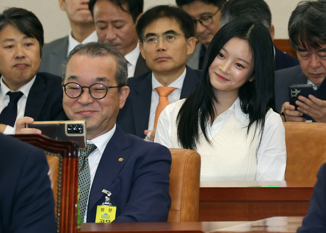 뉴진스 하니가 15일 서울 여의도 국회에서 열린 환경노동위원회 국정감사에서 회의 시작을 기다리고 있다. 스마트폰을 들고 사진을 찍는 증인이 정인섭 한화오션 거제사업장 사장이다. 국회사진기자단