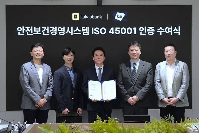 지난 15일 카카오뱅크 판교오피스에서 진행된 <안전보건경영시스템 ISO 45001 인증 수여식>에서 신희철 카카오뱅크 경영지원그룹장(왼쪽 세번째)과 고정석 총무팀장(왼쪽 첫번째), 조용진 매니저(왼쪽 두번째)가 임성환 BSI코리아 대표이사(오른쪽 두번째), 이승민 차장(오른쪽 첫번째)과 기념 촬영을 하고 있다. [사진 출처 = 카카오뱅크]