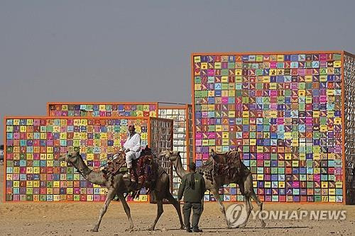 이집트 카이로 기자 피라미드 유적지에서 열린 '포에버 이즈 나우' 전시에서 낙타를 탄 관광 가이드가 강익중의 '네 개의 신전' 앞을 지나는 모습[AP=연합뉴스]