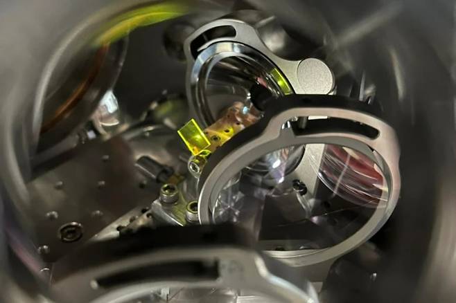 미국 국립표준기술연구소(NIST)와 콜로라도대 공동 연구진이 주파수 빗이라는 레이저 장치를 사용해 작은 흰색 원반의 결정에 박혀 있는 토륨-229의 핵에 레이저를 쏘고 있다./Ye Labs, JILA, NIST and Univ. Colorado