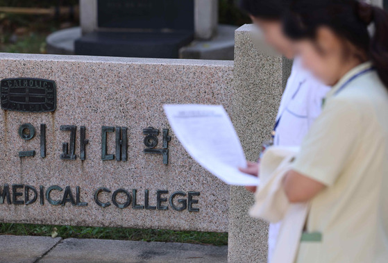 Two people walk by a plaque of medical college in downtown Seoul on Wednesday. [YONHAP]