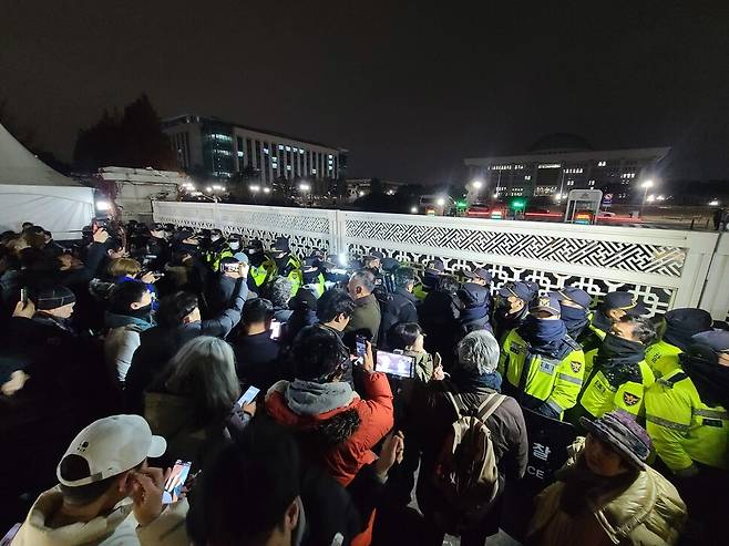 윤석열 대통령이 비상계엄을 선포한 3일 밤 경찰이 출입을 통제하는 서울 여의도 국회 들머리에서 시민들이 상황을 지켜보고 있다. 백소아 기자