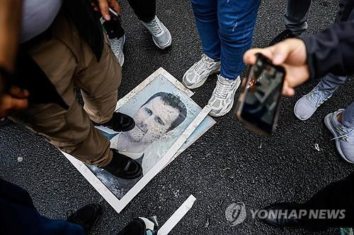 짓밟히는 알아사드 초상화 (이스탄불 AFP=연합뉴스) 8일(현지시간) 시리아 반군이 수도 다마스쿠스를 점령하자 튀르키예 이스탄불 주재 시리아 영사관 밖에 모인 시위대가 바샤르 알아사드 시리아 대통령 초상화를 발로 짓이기고 있다. 2024.12.8 photo@yna.co.kr