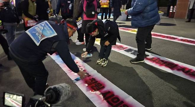민주노총 경남본부가 윤 대통령의 계엄령을 지지한 시의원이 있는 창원특례시의회 입구 앞 바닥에 ‘내란의 열차 탑승 국힘 창원 시의원 사퇴’ 등의 문구를 분사형 도로료 새기고 있다. 이세령 기자