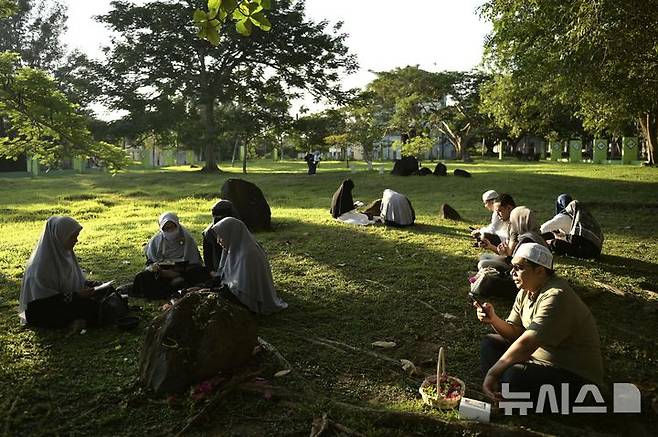 [AP/뉴시스] 인도네시아 북서단 아체주 주도 반다 아체에 있는 2004년 쓰나미 희생자 집단매장지 풀밭. 26일 20주년을 맞아 사람들이 모여 추모하고 있다.