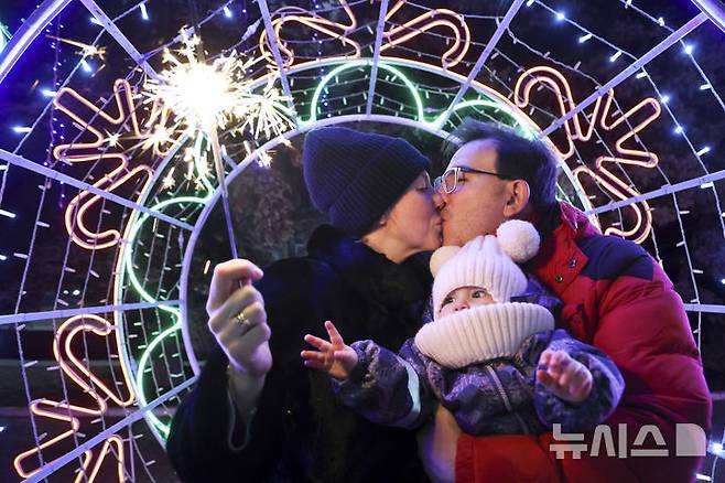 [도네츠크=AP/뉴시스] 지난해 12월 31일(현지시각) 우크라이나 동부 도네츠크 광장에서 아이를 안은 한 부부가 새해를 맞으며 입 맞추고 있다. 2025.01.01.