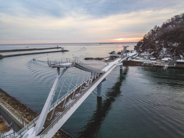 강원도 삼척시를 흐르는 오십천 하구 삼척항과 이사부 장군의 출항지로 추정되는 오분항을 잇는 보행 전용 ‘이사부 독도 평화의 다리’ 너머로 아침 해가 떠오르고 있다. 오른쪽에 오화리산성이 있는 고성산이 보인다.