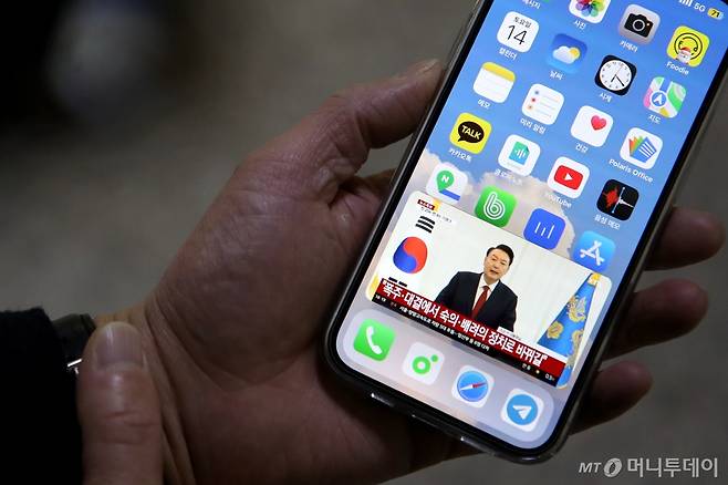 (윤석열 대통령 탄핵소추안이 가결된 14일 오후 서울 여의도 국회에서 한 직원이 윤 대통령의 '국민께 드리는 말씀'이라는 대국민 담화를 스마트폰으로 시청하고 있다./사진=서울=뉴스1) 이광호 기자