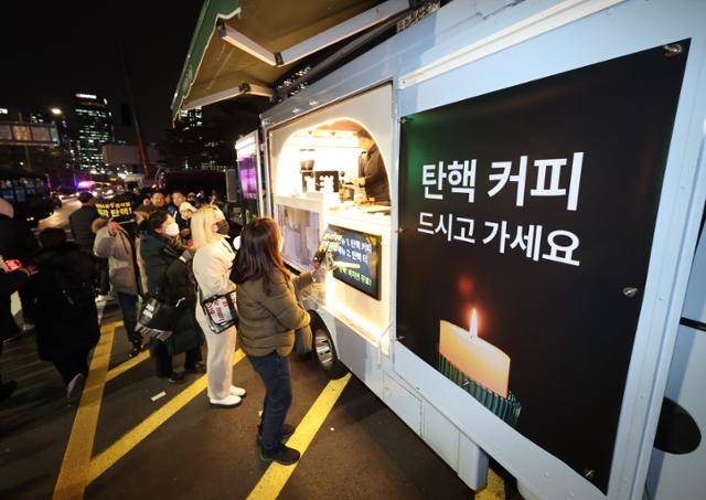 지난달 12일 오후 서울 영등포구 국회의사당 인근에서 열린 윤석열 대통령 탄핵 촉구 촛불 집회 행진에 참석한 시민들이 커피차에서 무료 음료를 기다리고 있다. 연합뉴스