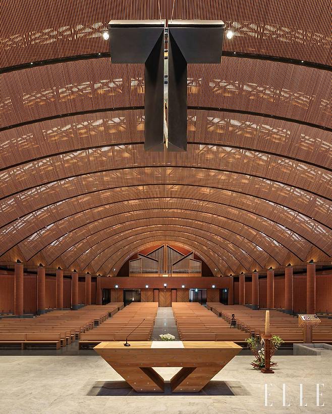 남양성모성지 대성당의 메인 홀은 곡선 천장이 특징이며, 나무 루버 사이로 들어오는 빛이 성스러운 분위기를 연출한다.