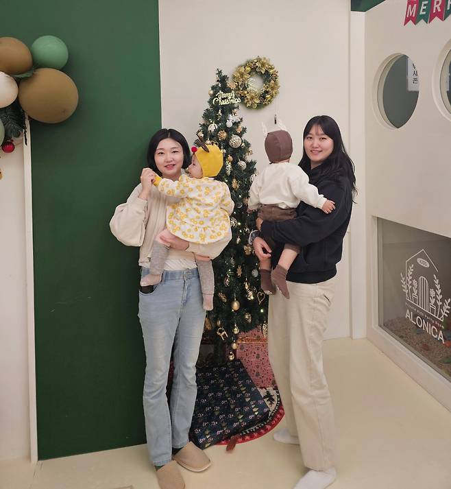 Yoon Sang-hee (left) and Lee Sun-hee pose for a photo, holding their babies in front of a Christmas tree inside a baby cafe. (Choi Jae-hee / The Korea Herald)