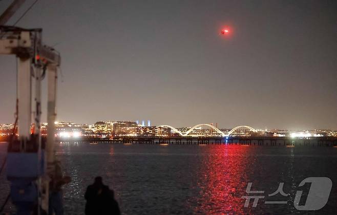 29일(현지시간) 버지니아주 알렉산드리아의 딩거필드에서 바라본 레이건 국립 공항 근처 포토맥강 상공에서 헬리콥터가 공중 추락 사고 생존자를 수색하고 있다. ⓒ AFP=뉴스1 ⓒ News1 류정민 특파원