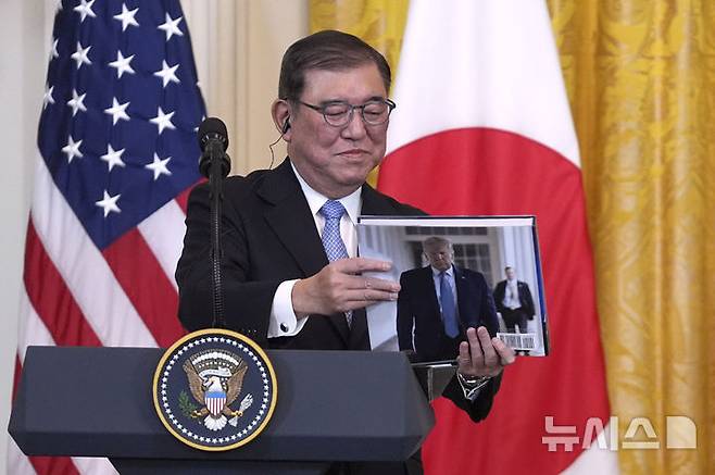 [워싱턴=AP/뉴시스] 이시바 시게루 일본 총리가 7일(현지 시간) 미국 백악관에서 열린 정상회담 후 공동 기자회견에서 도널드 트럼프 미국 대통령이 선물한 책을 들여다보고 있다. 2025.02.08.