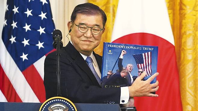 이시바 시게루 일본 총리가 지난 7일 미국 워싱턴 DC 백악관에서 도널드 트럼프 미 대통령이 선물한 사진첩을 들어 보이고 있다. 사진첩 표지는 지난해 7월 트럼프 당시 대선 후보가 펜실베이니아 야외 유세 도중 총격을 맞고 일어나 주먹을 들어 보이는 장면이다./AP 연합뉴스