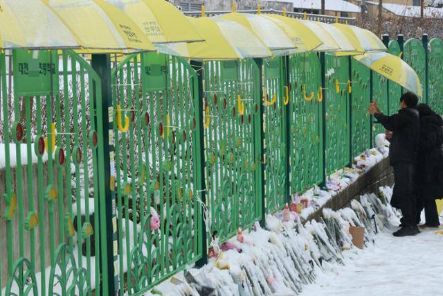 대전 초등학생 김하늘 양 피살사건이 발생한 대전 서구의 한 초등학교 정문에서 12일 오전 학교 관계자가 추모객들이 놓고 간 꽃과 편지 위에 우산을 씌워주고 있다. 학교 정문에는 시민들이 붙여 놓은 쪽지와 꽃, 인형, 선물들이 가득 차 있다. 대전=연합뉴스
