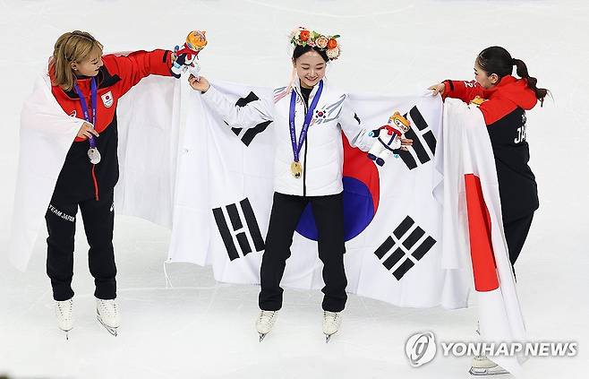 축하와 화합의 시간 (하얼빈=연합뉴스) 서대연 기자 = 피겨 김채연이 13일 중국 하얼빈 헤이룽장 빙상훈련센터 다목적홀에서 열린 하얼빈 동계아시안게임 피겨 여자 싱글에서 금메달을 획득, 은·동메달을 딴 일본 사카모토 가오리와 요시다 하나의 도움을 받아 태극기를 두르고 있다.
     김채연은 이날 경기에서 세계 1위 사카모토 가오리(일본)를 꺾고 금메달을 차지했다. 2025.2.13 dwise@yna.co.kr