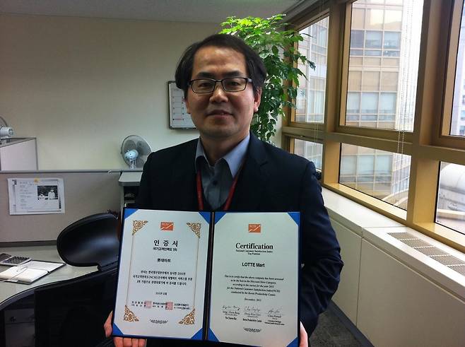 직장인 시절 롯데마트가 국가고객만족도 1위를 한 인증서를 들고 포즈를 취한 정선용 씨. 복장도 표정도 헤어스타일도 요즘과는 많이 다르다. 정선용 씨 제공