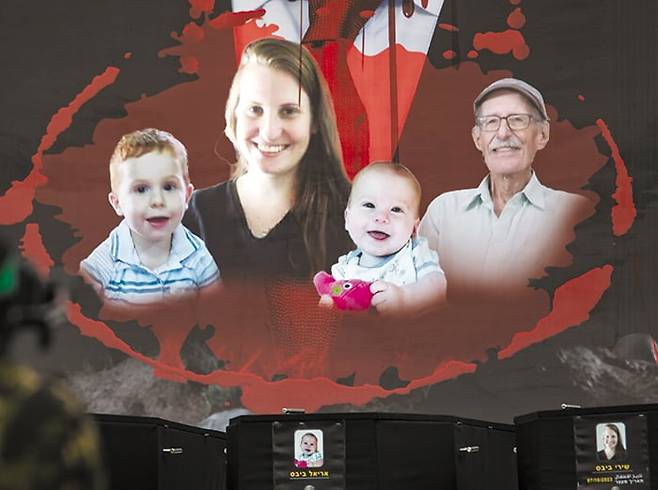 지난 20일 하마스가 이스라엘 인질 네 명의 시신이 담긴 관을 송환에 앞서 전시한 모습. 뒤편 현수막 왼쪽부터 아리엘·시리·크피르 비바스 일가족과 평화운동가 오데드 리프시츠. /EPA 연합뉴스