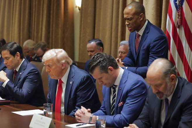 26일(현지시간) 미국 워싱턴 백악관에서 도널드 트럼프 대통령이 주재하는 첫 내각 회의(국무회의)를 시작하기에 앞서 스콧 터너 주택도시개발부 장관이 서서 대표 기도를 하고 있다. 트럼프 대통령(앞줄 왼쪽 두번쨰)과 마르코 루비오(앞줄 왼쪽 끝) 국무장관과 피트 헤게스(오른쪽 앞줄 두번째) 국방장관, 하워드 루트닉 상무부 장관이 고개를 숙이고 따라서 기도하고 있다. AP 연합뉴스