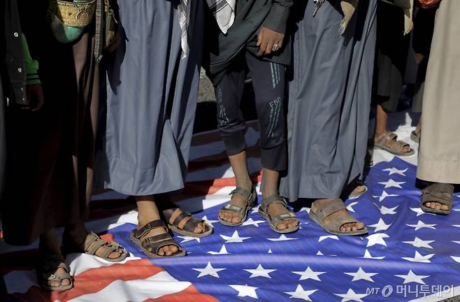 [사나=AP/뉴시스] 17일(현지 시간) 예멘 사나에서 열린 반미·반이스라엘 시위에 참석한 후티 반군 지지자들이 미국 국기를 밟고 있다. 2025.01.18. /